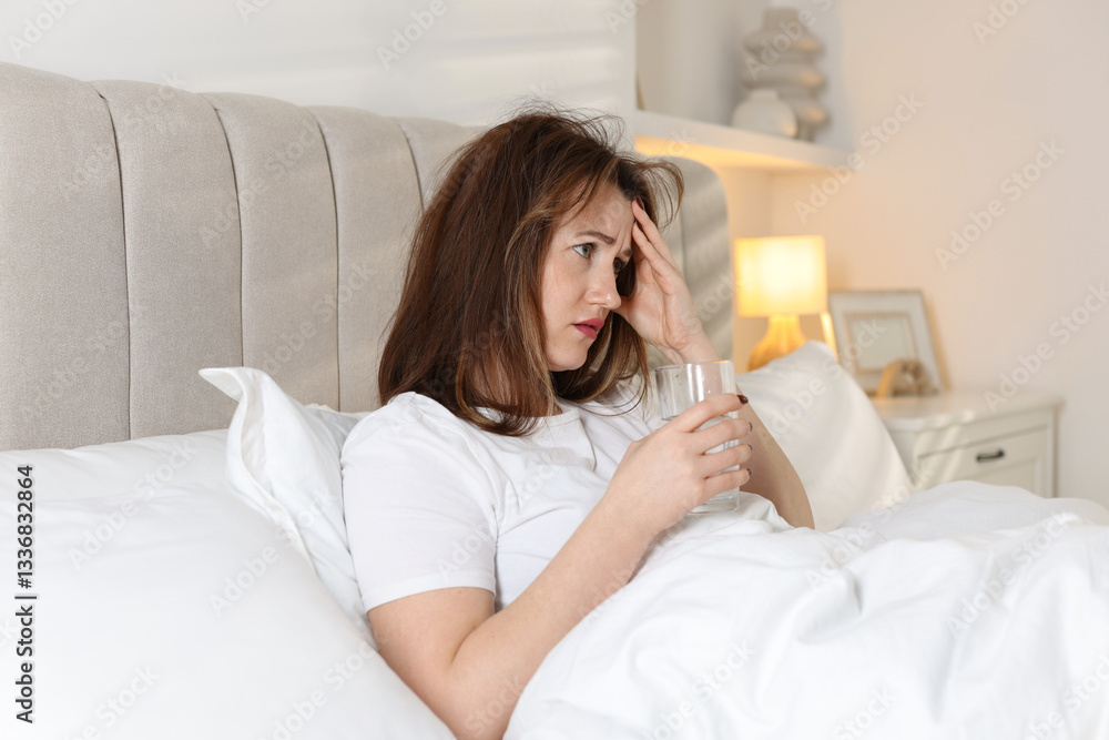 Unhappy woman with glass of water suffering from hangover on bed at home Unhappy woman with glass of water suffering from hangover on bed at home