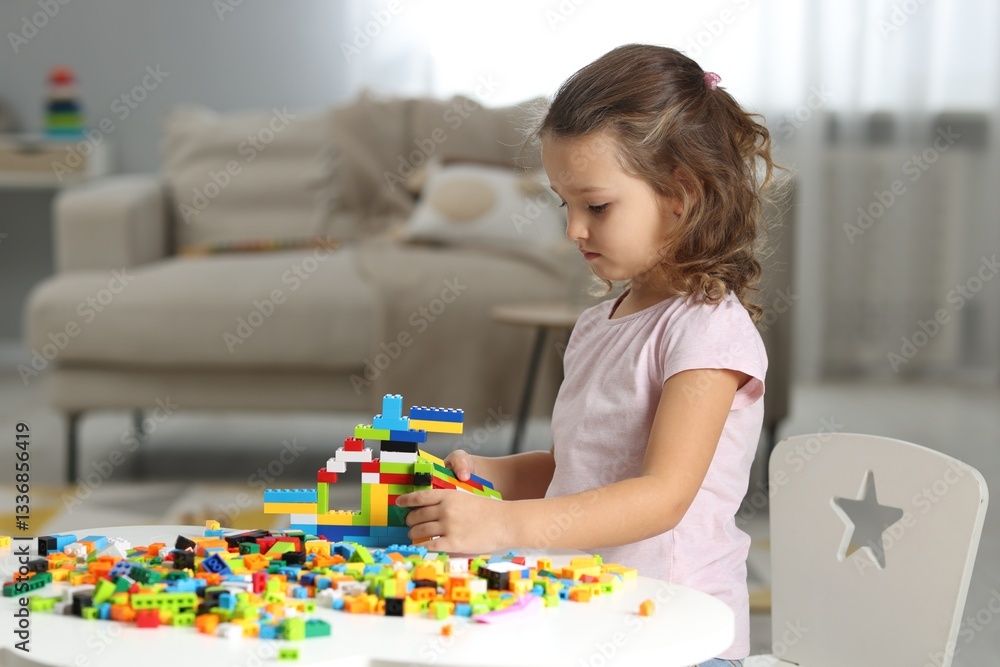 Fototapeta premium Cute girl playing with building blocks at white table indoors