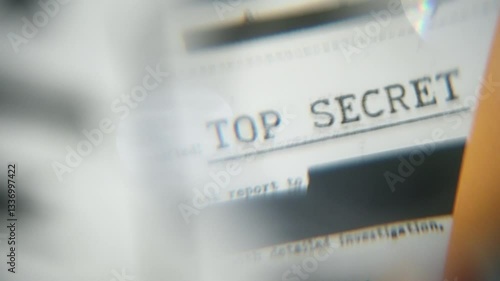 Abstract defocused close up with magnifying glass on Top Secret labeled on file. Confidential information and censored government report classified as Top Secret. Blacked out lines of censorship
