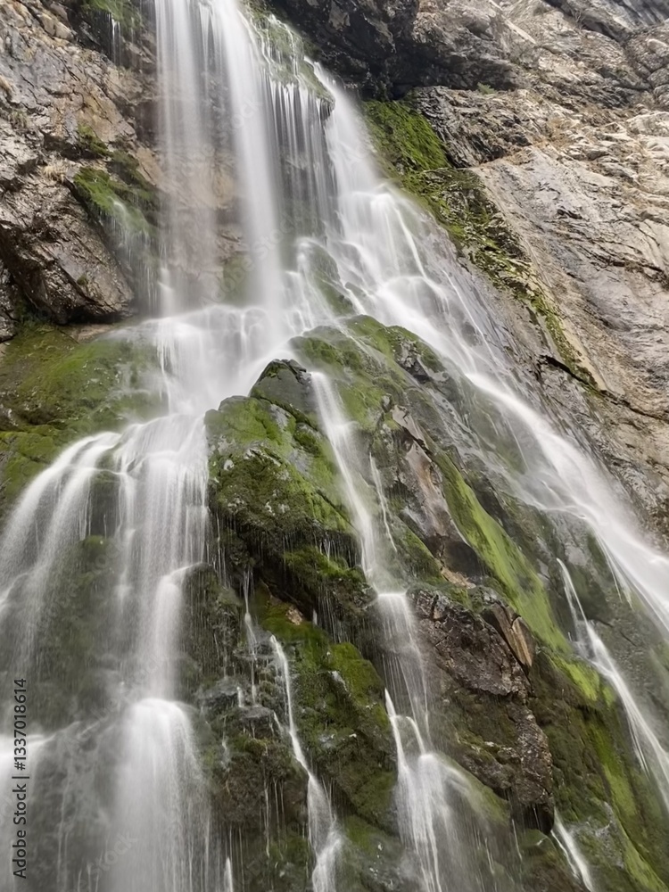 Fototapeta premium Waterfall cascading over moss-covered rocks on rugged cliffside