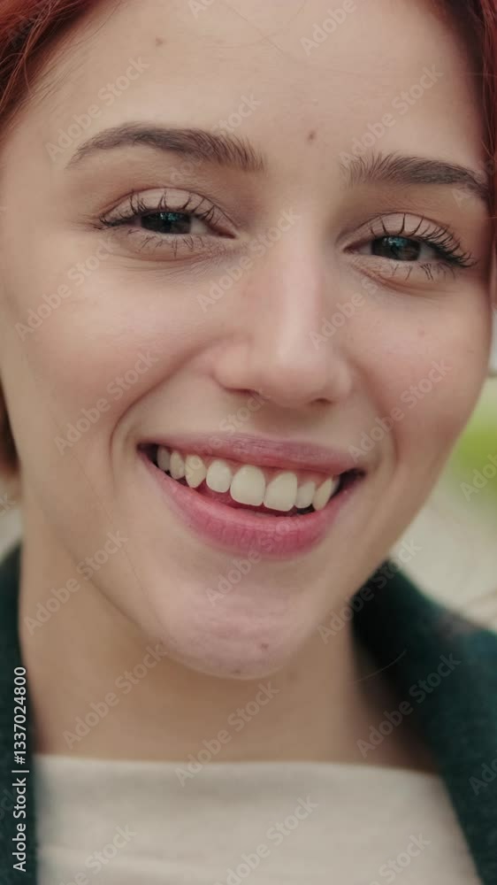 Vertical video, Happy young woman with red hair wearing wireless earbuds while walking and smiling in city street in slow motion. Vertical video, Happy young woman with red hair wearing wireless earbuds while walking and smiling in city street in slow motion.