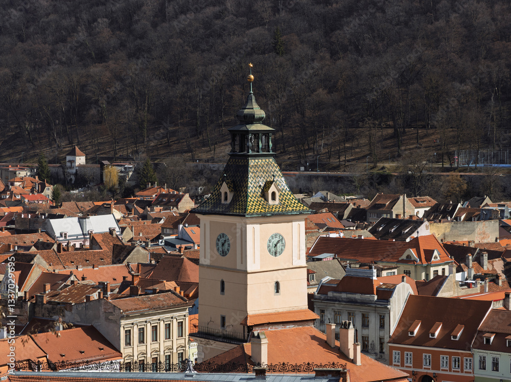 Fototapeta premium a detailed, elevated view of the Council Tower (Turnul Sfatului) in Brașov, Romania, set amidst the city's characteristic terracotta rooftops and against a backdrop of a forested mountain.
