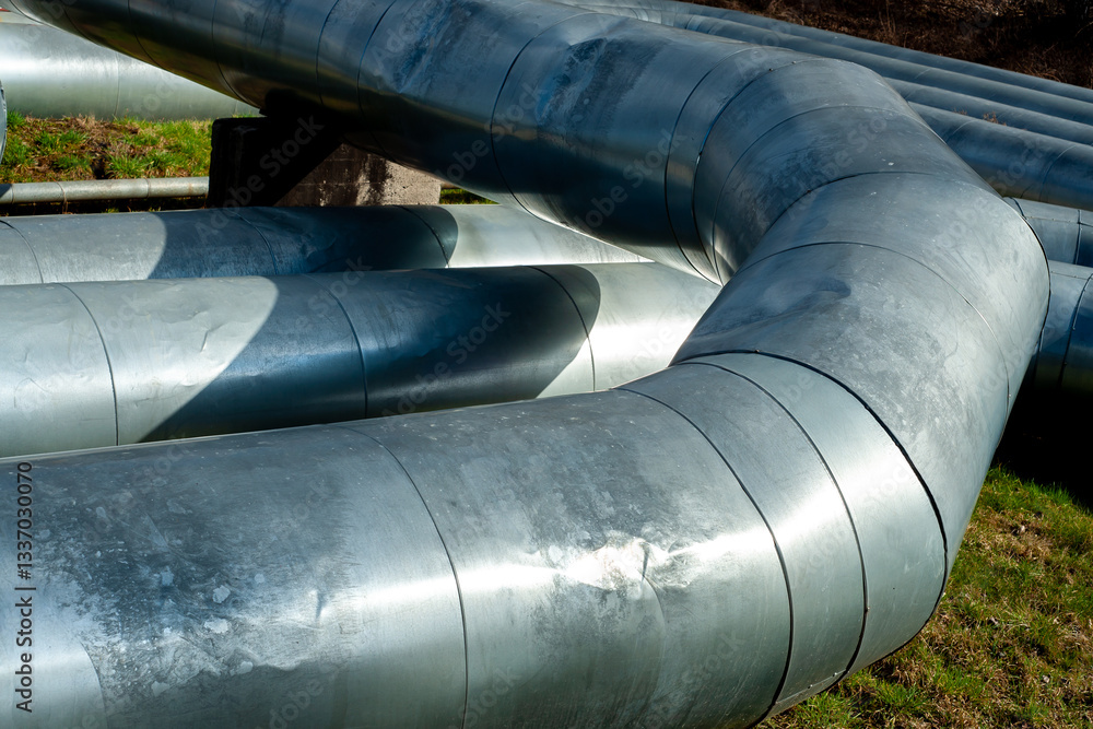 Close-up of curved insulated pipelines in an industrial setting. Metal surface and angles highlight the structure of an above-ground energy or heating distribution system Close-up of curved insulated pipelines in an industrial setting. Metal surface and angles highlight the structure of an above-ground energy or heating distribution system