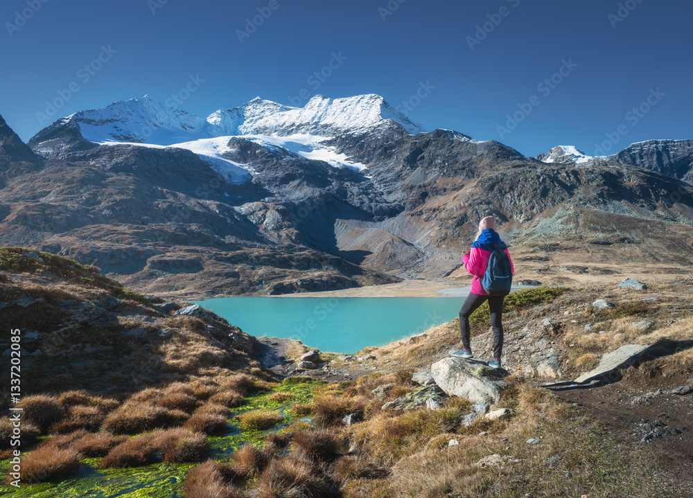 Φωτογραφία Young woman hiker with backpack standing on a rock admiring a beautiful turquoise alpine lake with snowy mountain and glacier in the background in fall