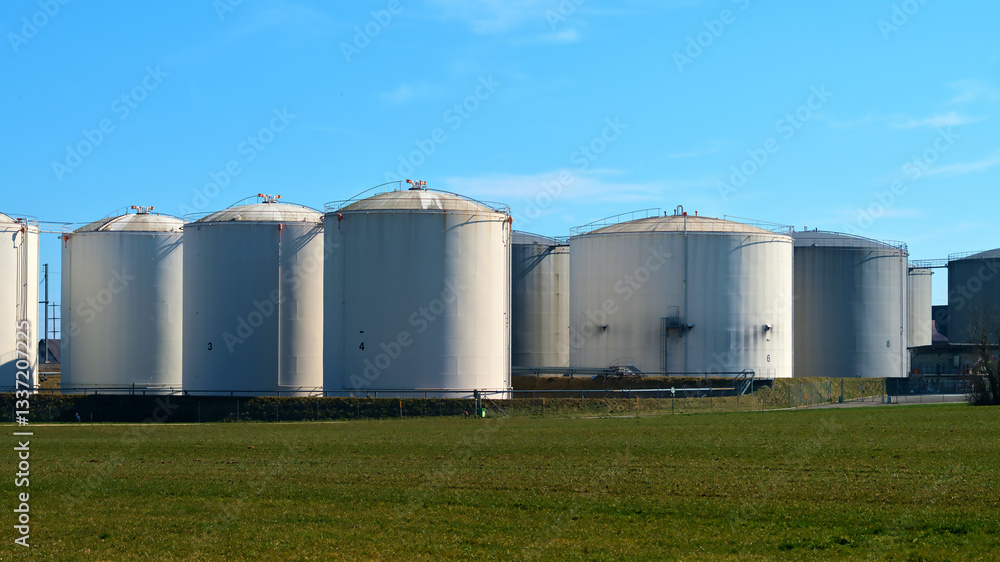 Large storage tanks at an industrial site surrounded by green fields under a clear blue sky during midday Large storage tanks at an industrial site surrounded by green fields under a clear blue sky during midday