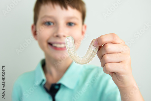 Smiling teenage boy holding aligners, silicone cap for teeth straightening. Orthodontist correcting bite.