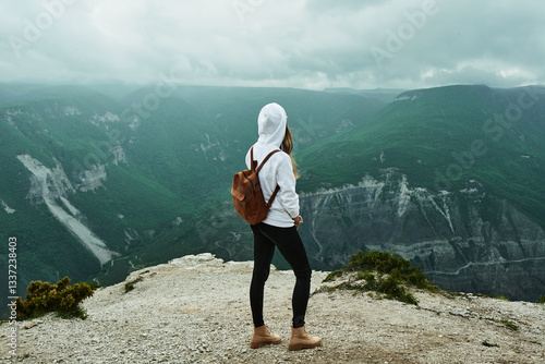 Young woman traveler in white sweatshirt with backpack on her back enjoying view of Sulak canyon. Republic of Dagestan, Russia. Freedom, travel, lifestyle concept.