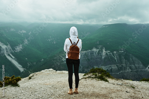 Young woman traveler in white sweatshirt with backpack on her back enjoying view of Sulak canyon. Republic of Dagestan, Russia. Freedom, travel, lifestyle concept.