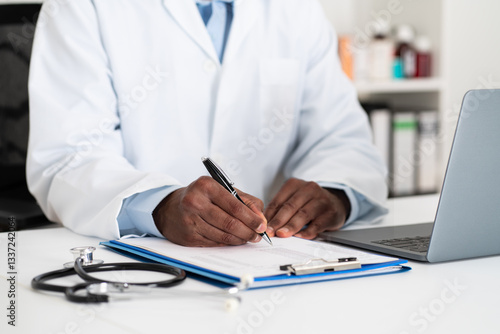 Close-up of doctor hands writing on paper or document at a desk in the hospital.Healthcare professional drafting a medical insurance letter, legal paperwork or form.A GP filing a document in a clinic