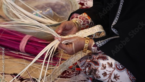 Emirati woman weaving traditional basket from palm leaves, hands in frame