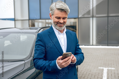 Businessman using his smartphone while standing at dealership