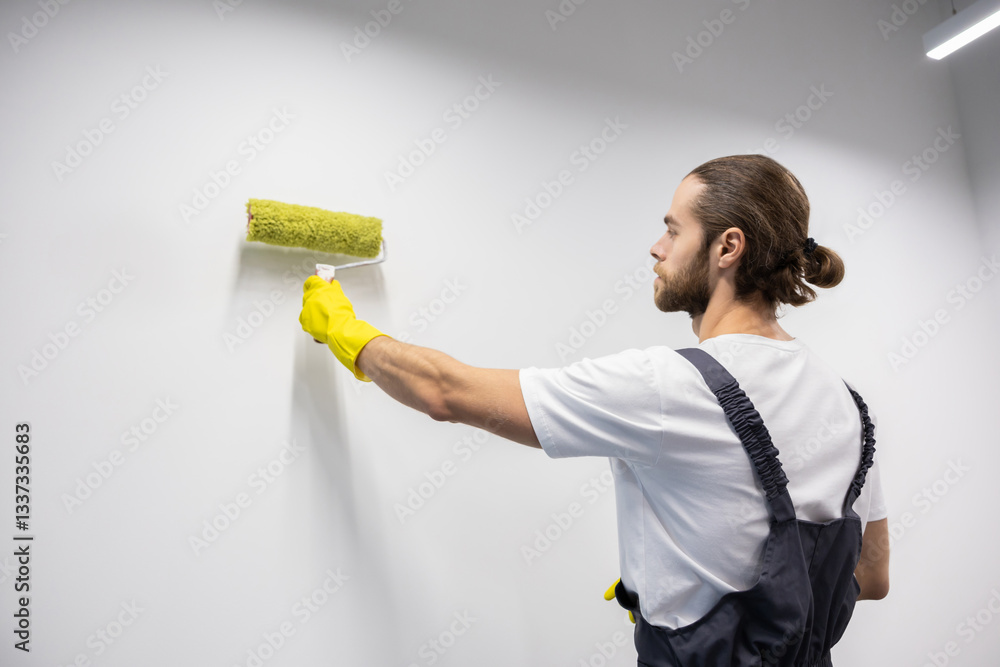 Dark-haired young bearded man in yellow gloves painting the wall Dark-haired young bearded man in yellow gloves painting the wall