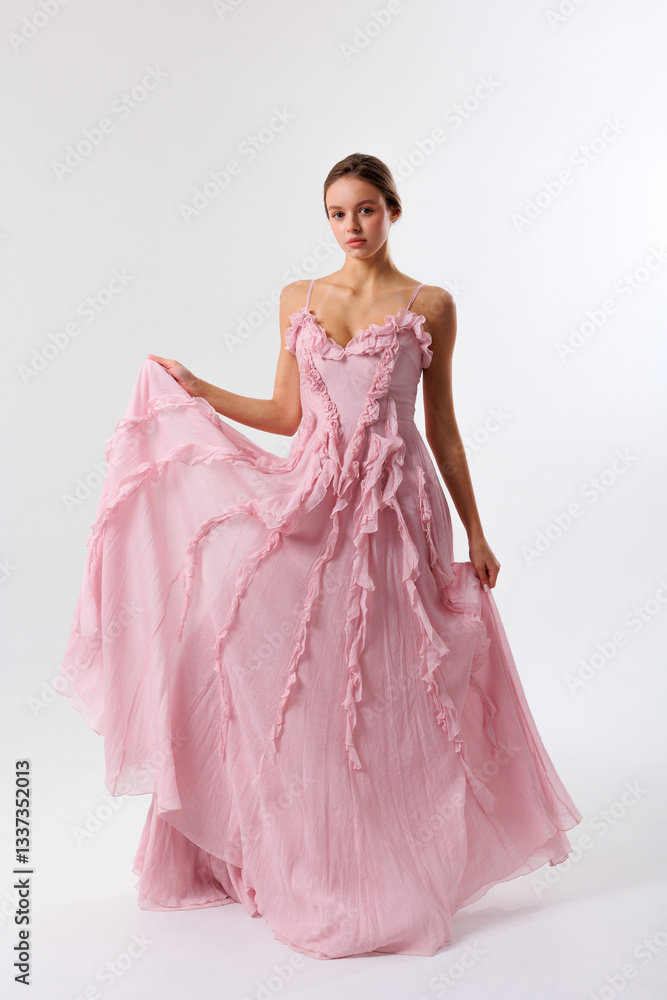 Fototapeta premium Elegant model showcasing a flowing pink gown in a minimalist studio setting during a fashion shoot