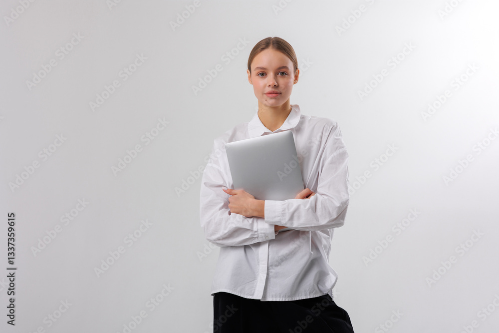 Young woman holding laptop in white shirt poses confidently against a bright background Young woman holding laptop in white shirt poses confidently against a bright background
