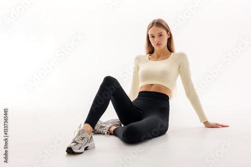 Stylish fitness model poses in comfortable activewear on a bright, minimalistic background during a studio photoshoot