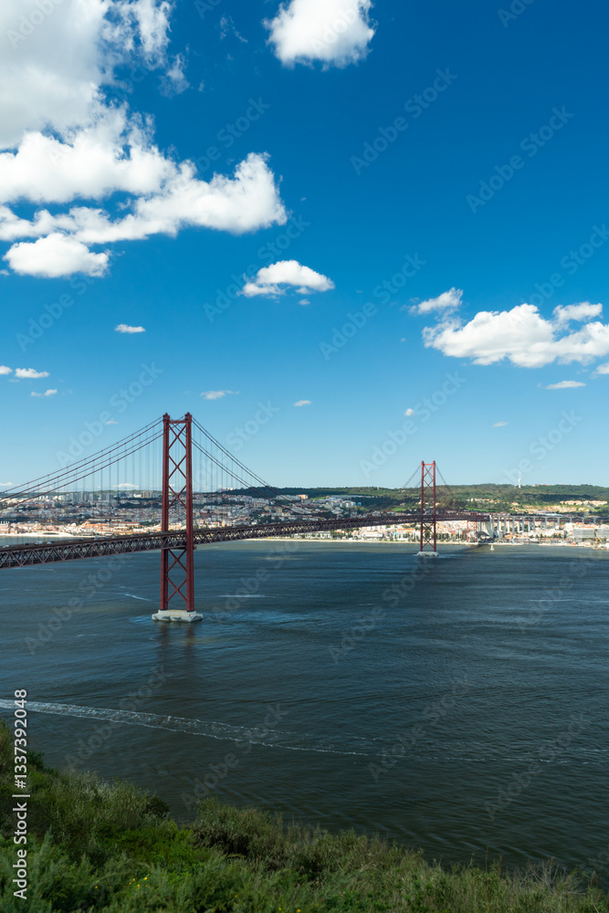 25th of April Bridge. Ponte 25 de Abril Suspension Bridge and Lisbon Skyline. Blue Sky and Cumulus Fluffy Clouds. Portugal 25th of April Bridge. Ponte 25 de Abril Suspension Bridge and Lisbon Skyline. Blue Sky and Cumulus Fluffy Clouds. Portugal