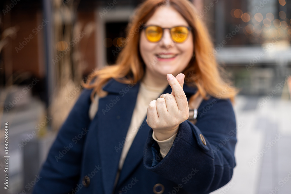 Female hand showing finger heart or mini heart gesture with the index finger and thumb come together like a snap outdoors. 30s Woman in sunglasses on urban background. High quality photo.