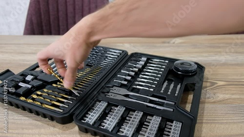 Choosing Drill Bit from Box of New, Shiny Drill Bits on Wooden Desk