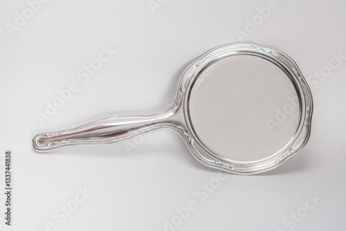 An antique hand mirror featuring a ornate silver handle and a round reflective surface. The mirror shows signs of aging and wear, adding to its vintage charm, mirror on white background