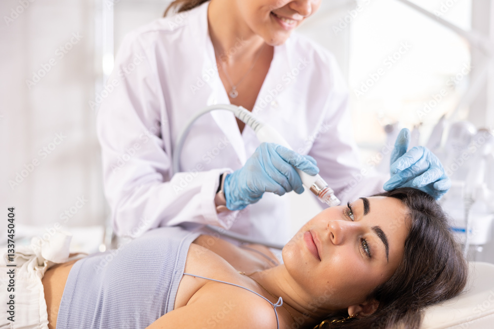 Young girl receiving facial procedure with attachment producing water with hydrogen and oxygen ions, ensuring deep penetration into dermis, relieving skin of blackheads. Modern hardware cosmetology Young girl receiving facial procedure with attachment producing water with hydrogen and oxygen ions, ensuring deep penetration into dermis, relieving skin of blackheads. Modern hardware cosmetology