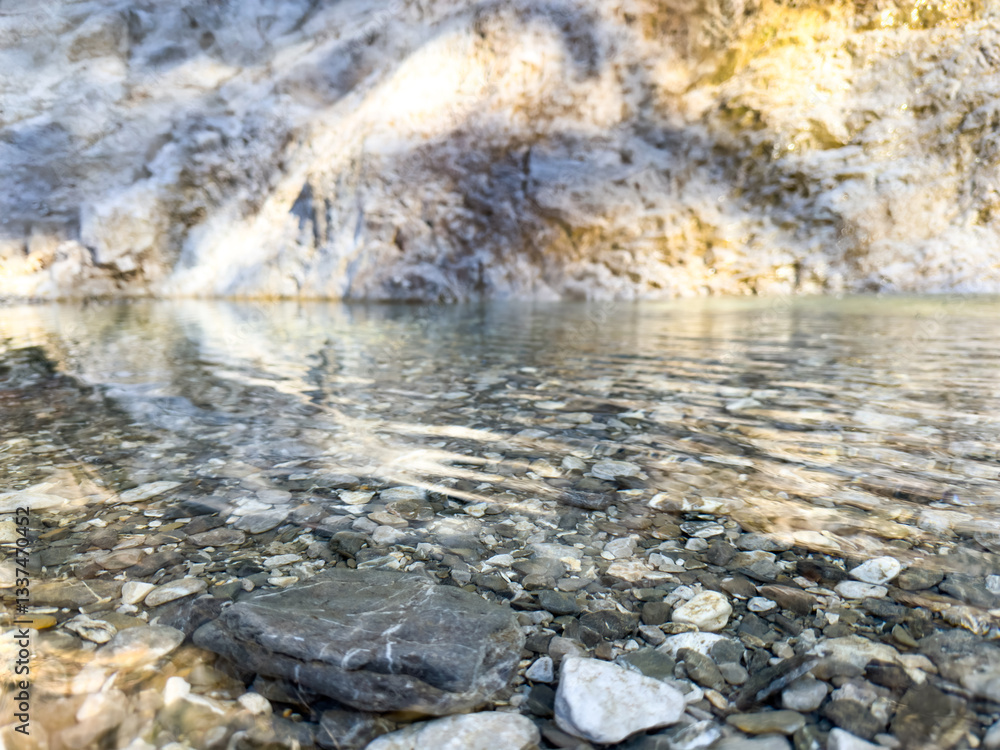 Obraz premium mountain river with crystal clear water and visible stones under the surface. natural landscape with soft sunlight reflections and rocky