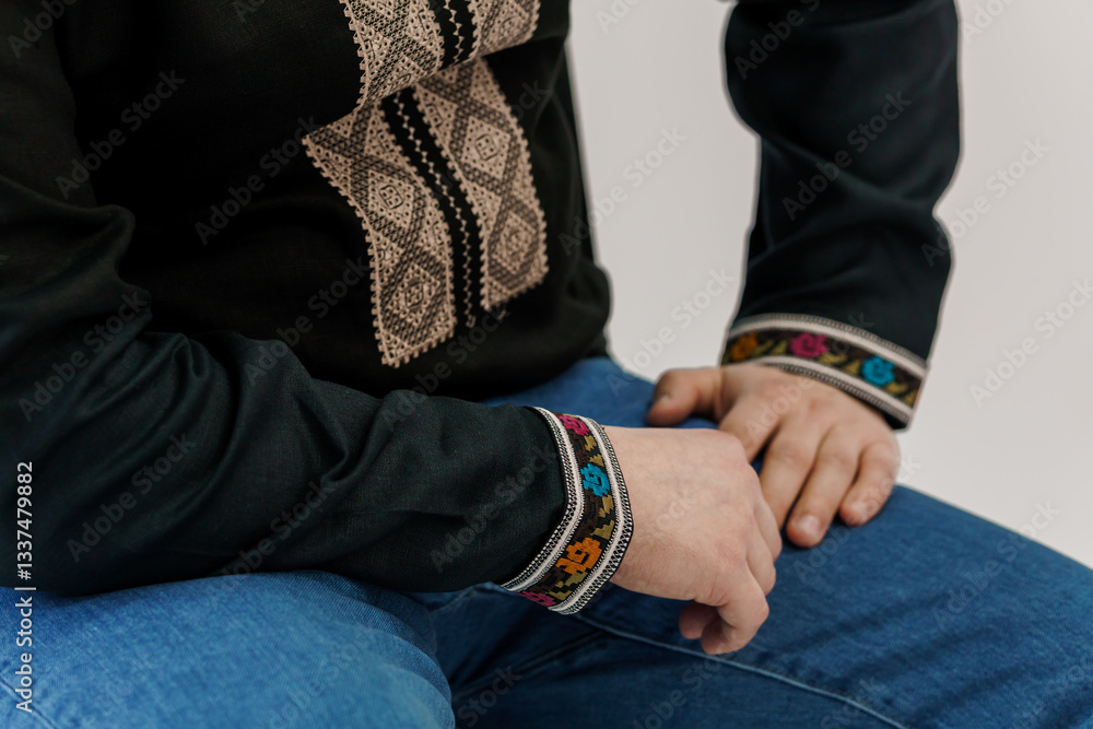 Fototapeta premium Close-Up View of Person Wearing Traditional Dark Blouse with Detailed Ornamental Embroidery on Chest and Sleeves Paired with Blue Jeans