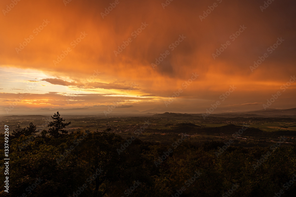 vista panoramica su parte del territorio tra pianura e collina, nella regione Friuli Venezia Giulia, dopo un temporale estivo, al tramonto, con le nuvole colorate di arancione dalla luce del sole