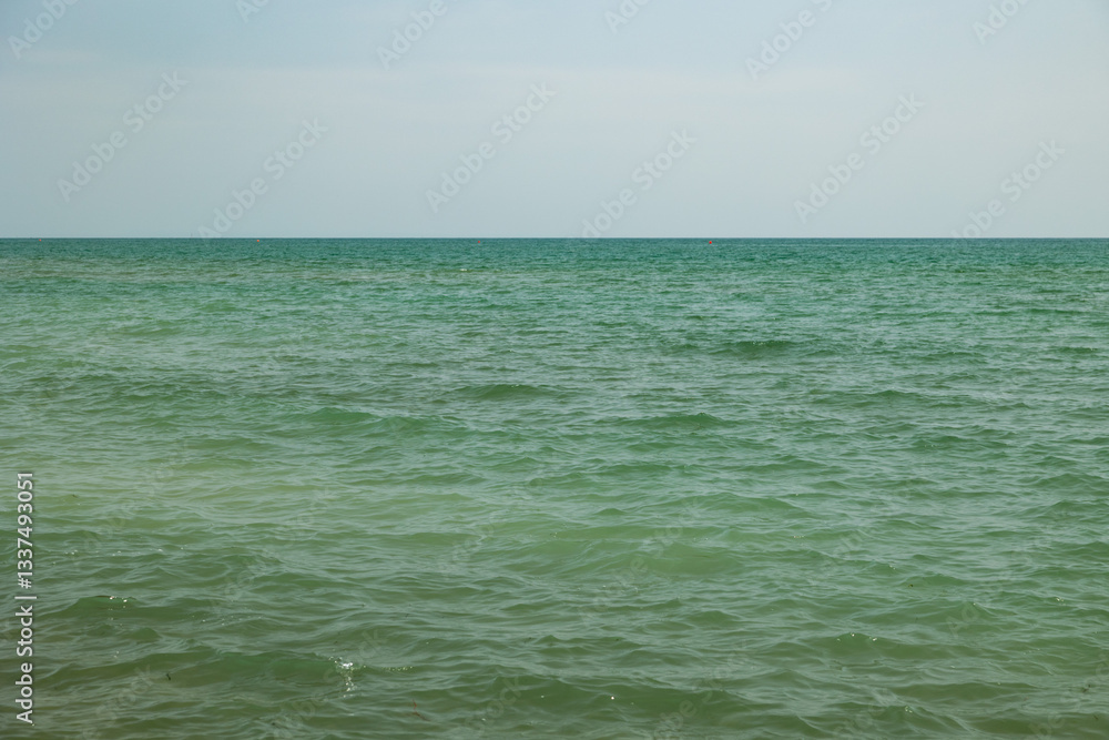 vista dettagliata del mare Adriatico calmo, di giorno, in estate, con cielo velato da una leggera foschia