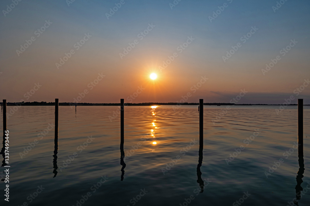 tramonto su una laguna in un ambiente marino tranquillo, nella regione Veneto, con cielo sereno, in estate, che si riflette sull'acqua
