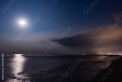 panoramica notturna su un ambiente marino sul mare Adriatico, dalla costa della regione Veneto, con mare calmo, mentre la luna si riflette sull'acqua, in estate, con vista su una città lontana