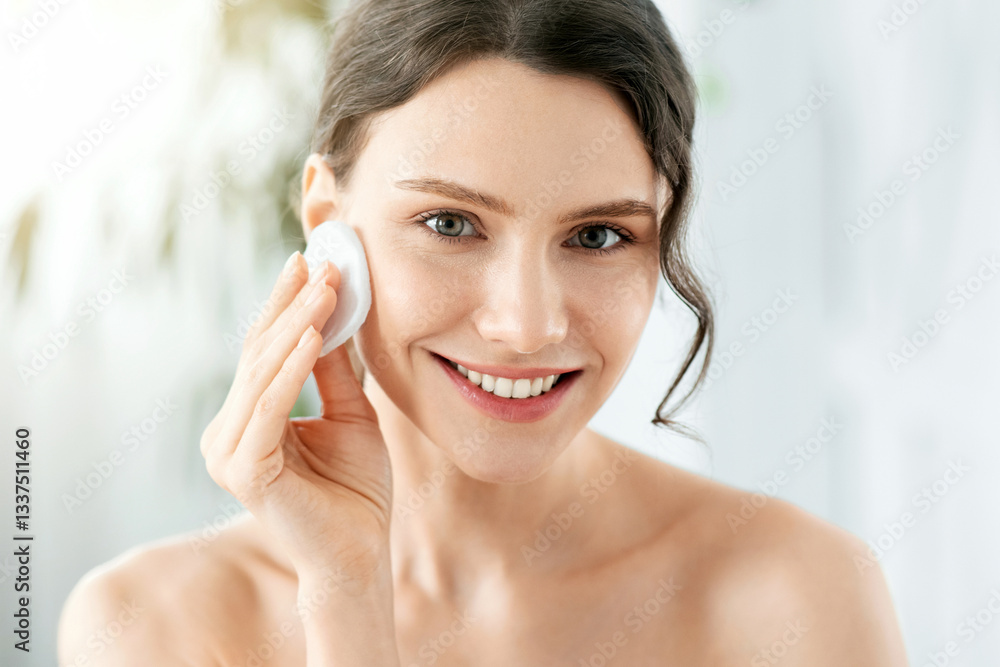 Smiling pretty young woman cleaning her face, using cotton pads and cleansing product, closeup. Young attractive lady using face toner and cotton pad, home interior, empty space, face care products Smiling pretty young woman cleaning her face, using cotton pads and cleansing product, closeup. Young attractive lady using face toner and cotton pad, home interior, empty space, face care products