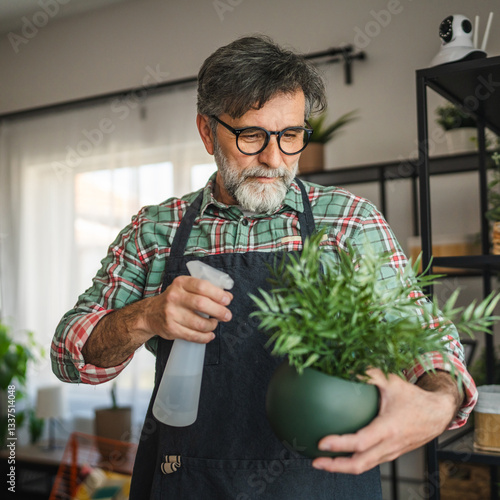 Fotografie mature male gardener take care of potted plant and watering with spray
