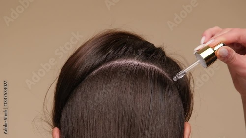 Beautiful woman with brown healthy hair applying oil or serum to roots on beige background. Hair beauty