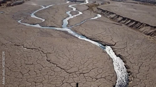 Aerial view of a person standing alone on cracked, arid land with a diminishing river flowing through the barren landscape, highlighting themes of drought and climate change.