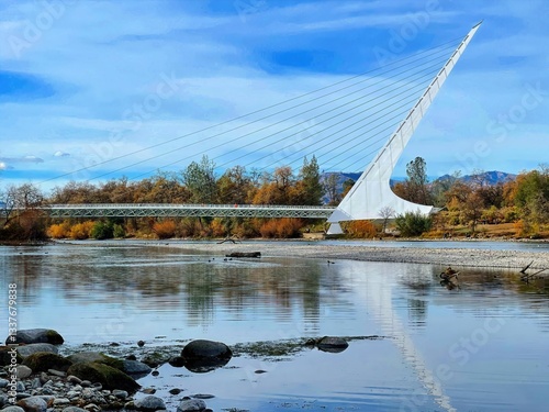 Foto Sundial Bridge Redding Autumn: Sundial Bridge’s white structure reflects in the Sacramento River, surrounded by fall foliage, ideal for nature and architecture
