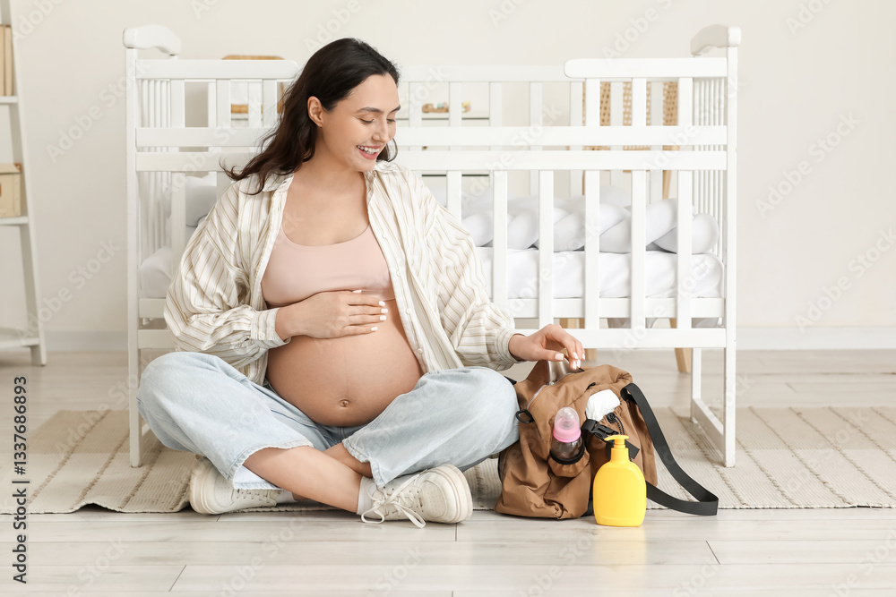 Φωτογραφία Young pregnant woman with maternity hospital bag sitting in children's bedroom