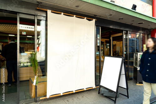 White curtain hanging in entrance of restaurant with glass doors, blank signboard outside, street view, urban setting, casual atmosphere, people walking by, Japanese style.