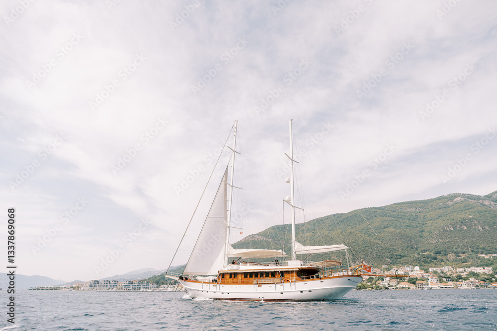 Luxury sailing yacht sails on the sea against the backdrop of green mountains Luxury sailing yacht sails on the sea against the backdrop of green mountains