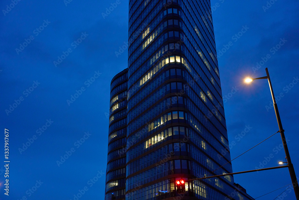 Modern glass skyscraper with illuminated office windows against night sky. High-rise office building with glowing lights in nighttime cityscape