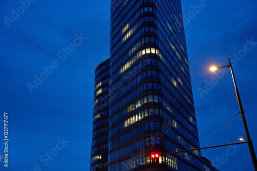 Modern glass skyscraper with illuminated office windows against night sky. High-rise office building with glowing lights in nighttime cityscape