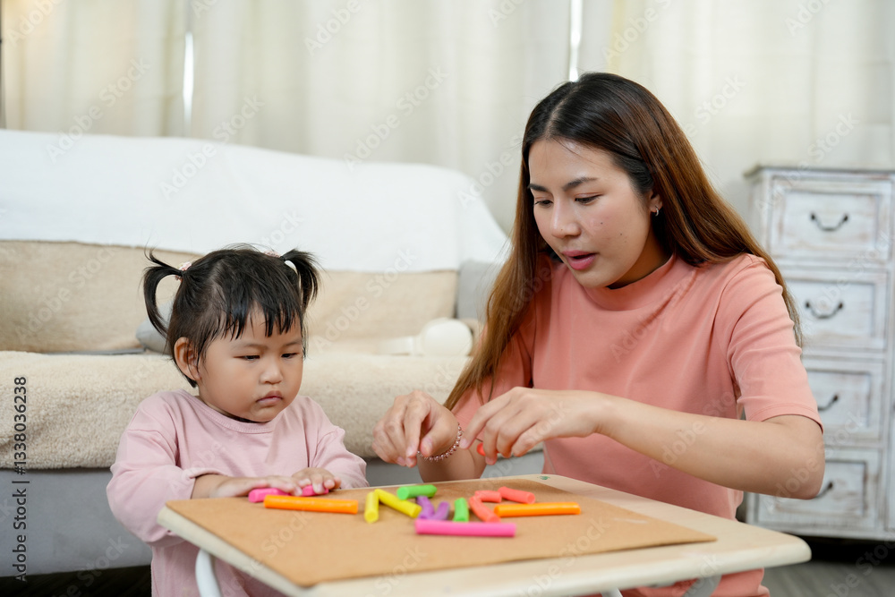 Single mother teaching young daughter at home through hands-on learning. Sitting together at small table arranging colorful foam pieces. Warm and loving home environment fostering early education. Single mother teaching young daughter at home through hands-on learning. Sitting together at small table arranging colorful foam pieces. Warm and loving home environment fostering early education.