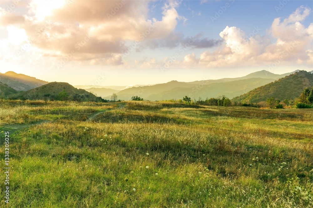 Fototapeta premium beautiful green valley with green fields with green spring grass with nive hills and mountains and scenic colorful cloudy sunset on background of landscape