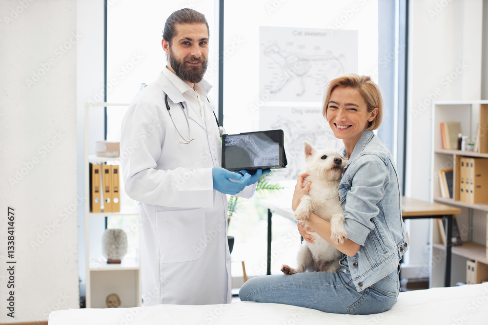 Obraz premium Young adult male veterinarian showing medical results to female pet owner with dog indoors. Bright office environment displaying animal anatomy charts in background.