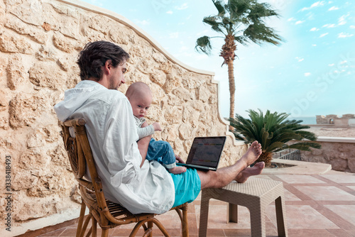 dad and his little son with a laptop are resting and working as a freelancer on vacation