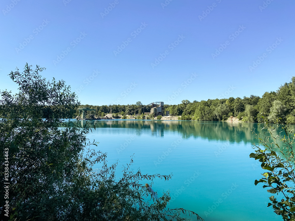Obraz premium Beautiful lake with a blue sky in the background. The water is calm and clear. Trees are surrounding the lake, creating a peaceful and serene atmosphere