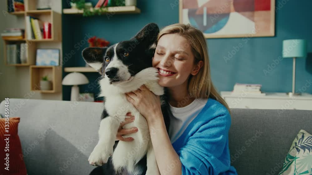 Radiant Caucasian woman lifting curious corgi while sitting on stylish couch. Smiling joyfully and embracing playful pet in bright cozy living room filled with warm decorative accents. Radiant Caucasian woman lifting curious corgi while sitting on stylish couch. Smiling joyfully and embracing playful pet in bright cozy living room filled with warm decorative accents.
