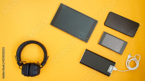 Bild auf Leinwand Flat lay of black tablet, smartphones, headphones, and power bank on a yellow surface