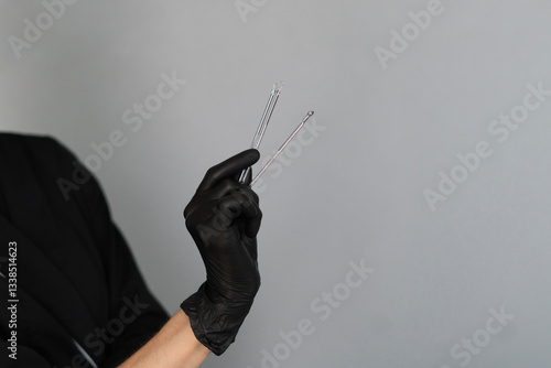 A cosmetologist dressed in black gloves holds various instruments designed for skin cleaning, ready to provide a facial treatment in a tranquil setting