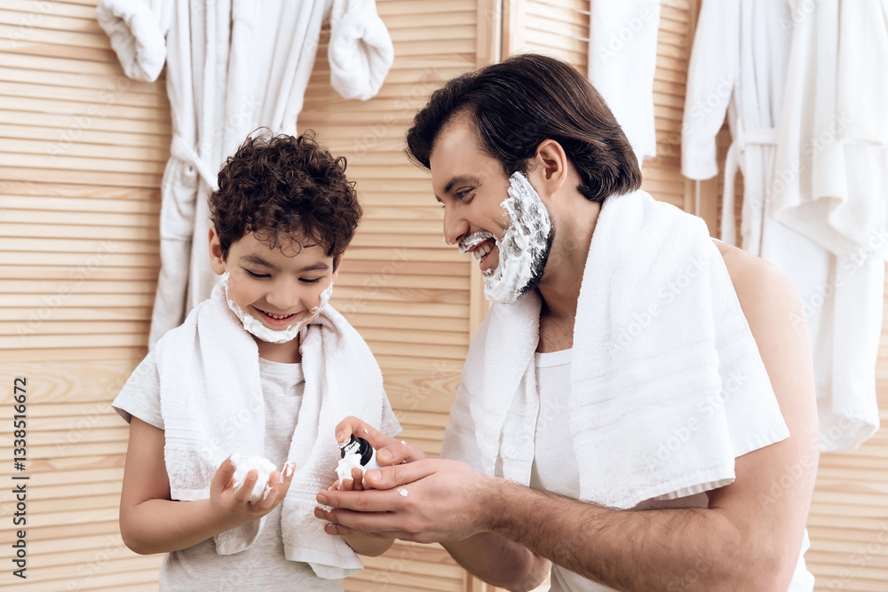 Joyful father inserts shaving foam onto hands of young son. Joyful father inserts shaving foam onto hands of young son.