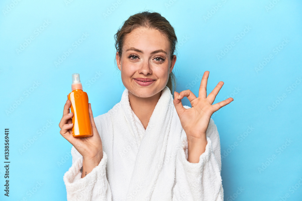 Blonde in bathrobe with sunscreen cream in studio cheerful and confident showing ok gesture. Blonde in bathrobe with sunscreen cream in studio cheerful and confident showing ok gesture.